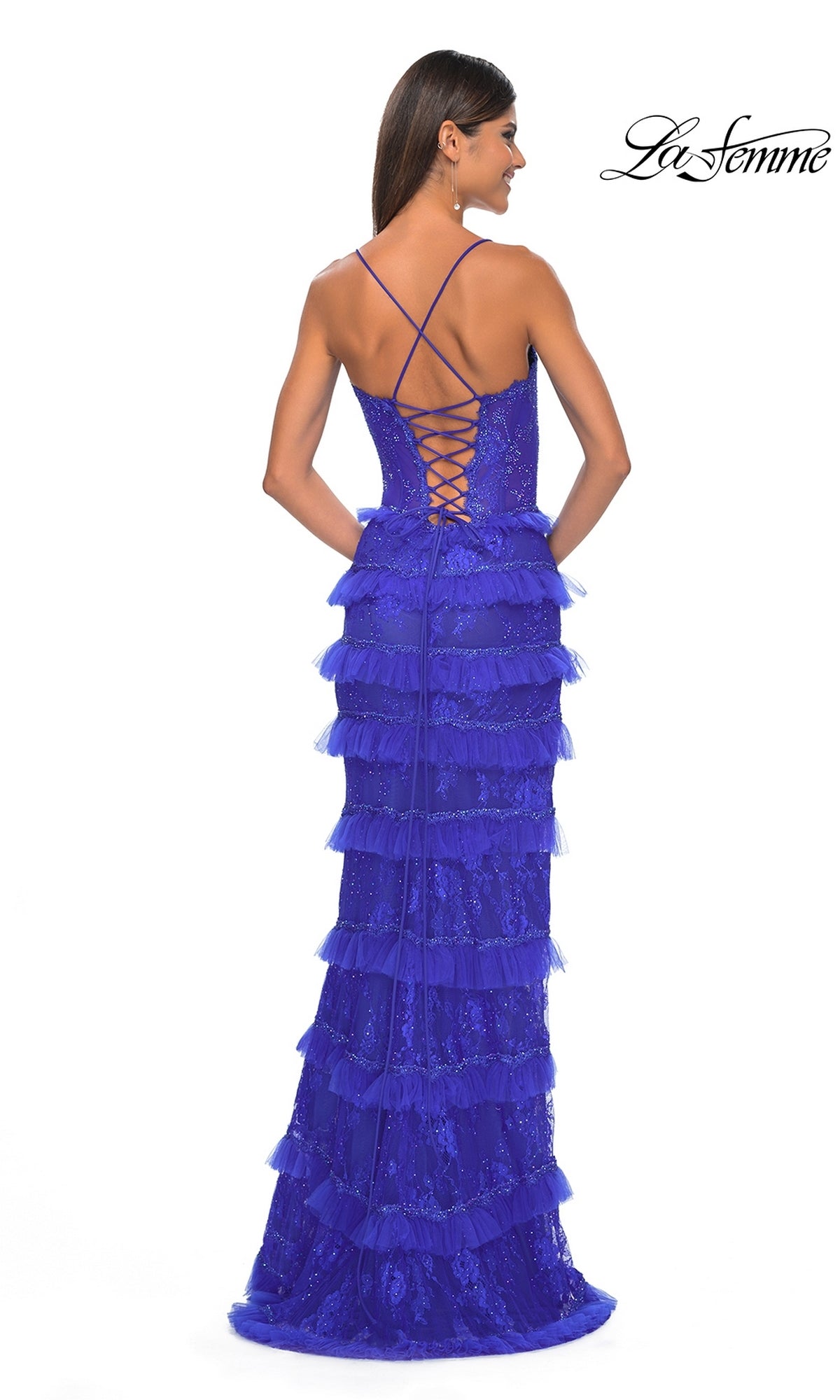 A woman models the Ruffled Long Beaded-Lace Prom Dress: La Femme 32442, featuring sleeveless, floor-length ruffled layers and royal blue beaded lace with a lace-up back, set against a white background.